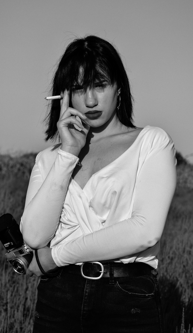 Žena u bijeloj bluzi s cigaretom i fotoaparatom